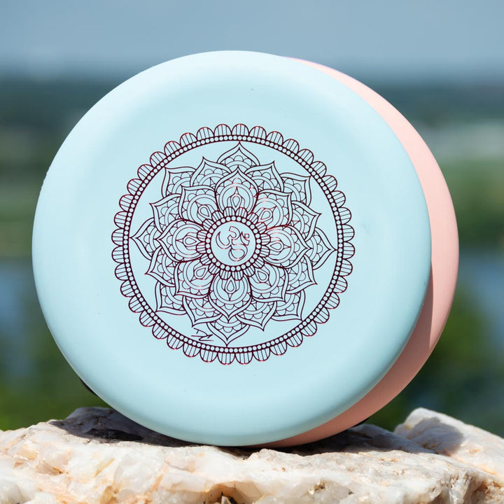 The Wizard - Mandala is a round disc container featuring an intricate mandala design on the lid, set on a rock outdoors with a soft-focus natural background. Ideal for storing flight numbers or noting your collection's 160-Max weight.