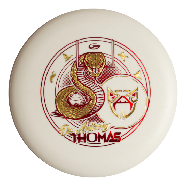 The De'Anthony Thomas' Wizard - SS - Superglow is a white disc golf disc featuring a gold snake, football goalpost, stylized mask, and "De'Anthony Thomas" in gold/red lettering€”perfect for Cardinal Disc Golf fans.