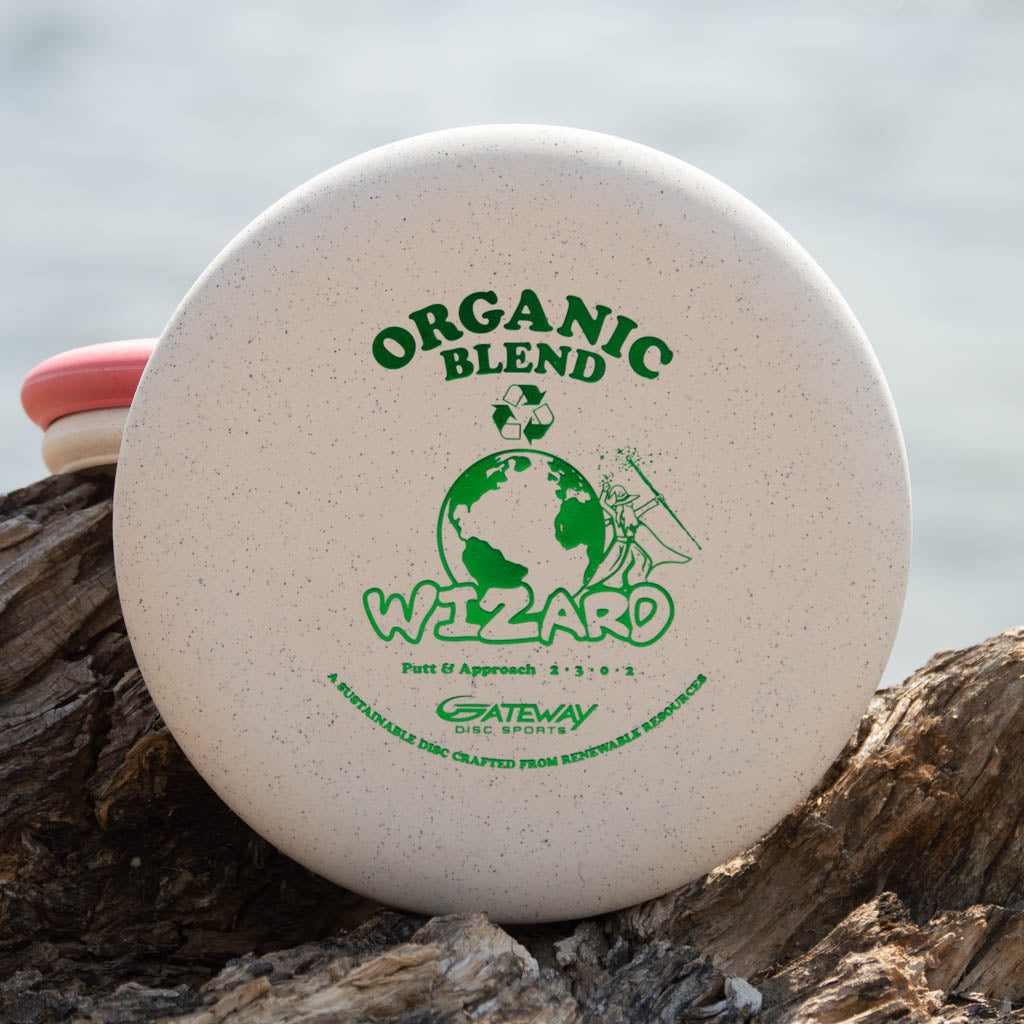 A white stable Wizard - SSSS - Hemp putter by Gateway Disc Sports rests on a piece of wood near water.