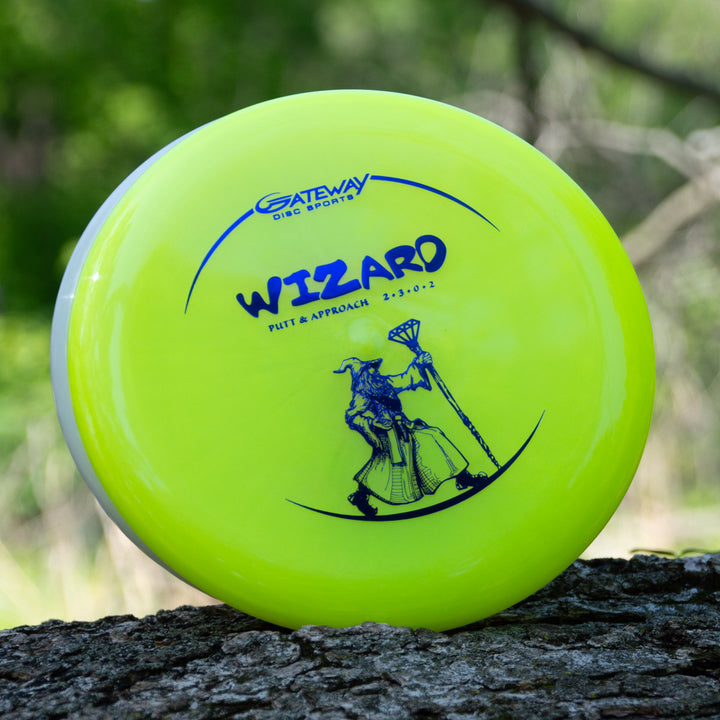 A yellow Gateway Wizard - Diamond overstable putt and approach disc, featuring a wizard with a staff, is seen resting on a tree trunk outdoors.