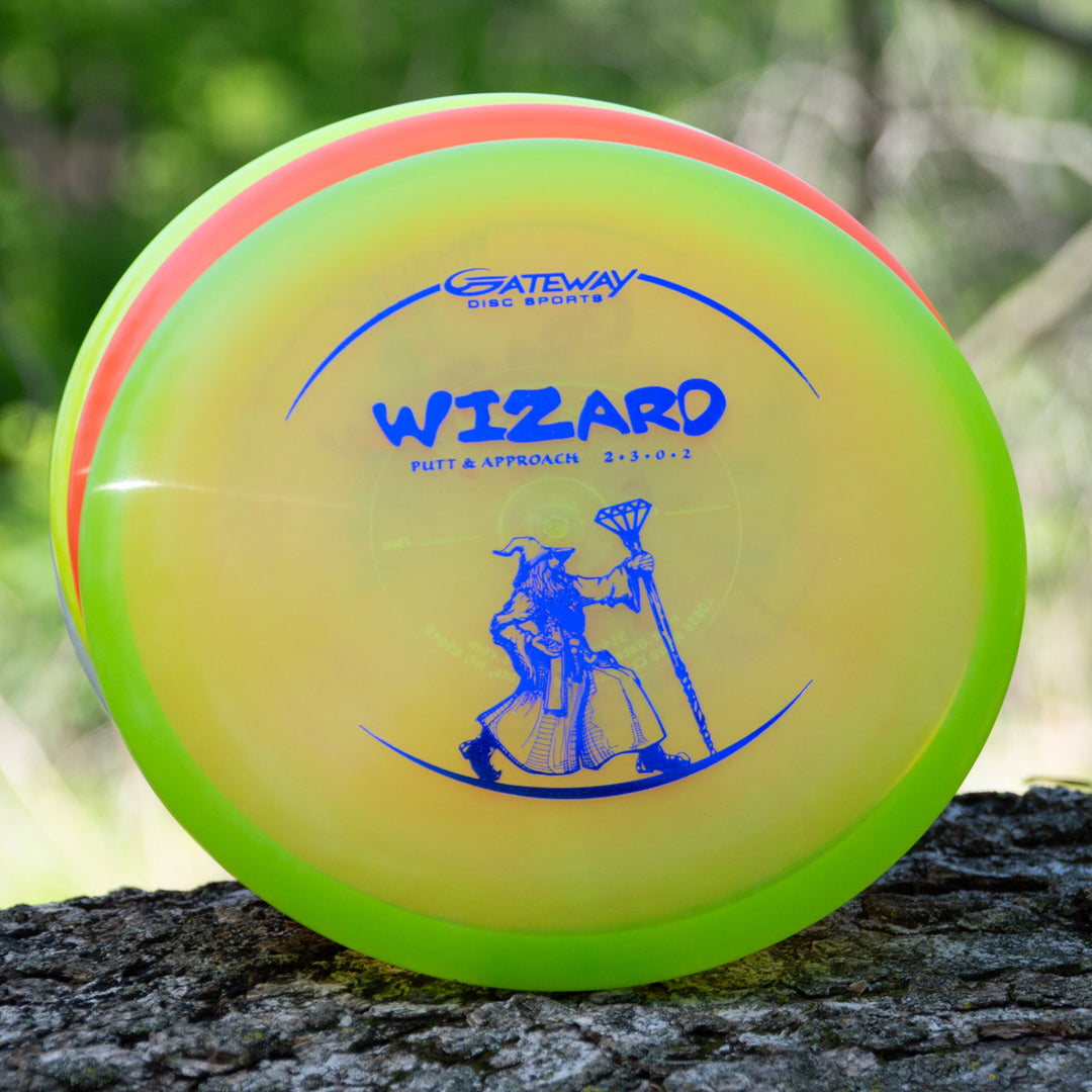 A yellow and green overstable Wizard - Diamond disc golf putter with a blue wizard design and flight numbers 2-3-0-2 rests on a tree trunk—an ideal, reliable putt and approach disc for any player.