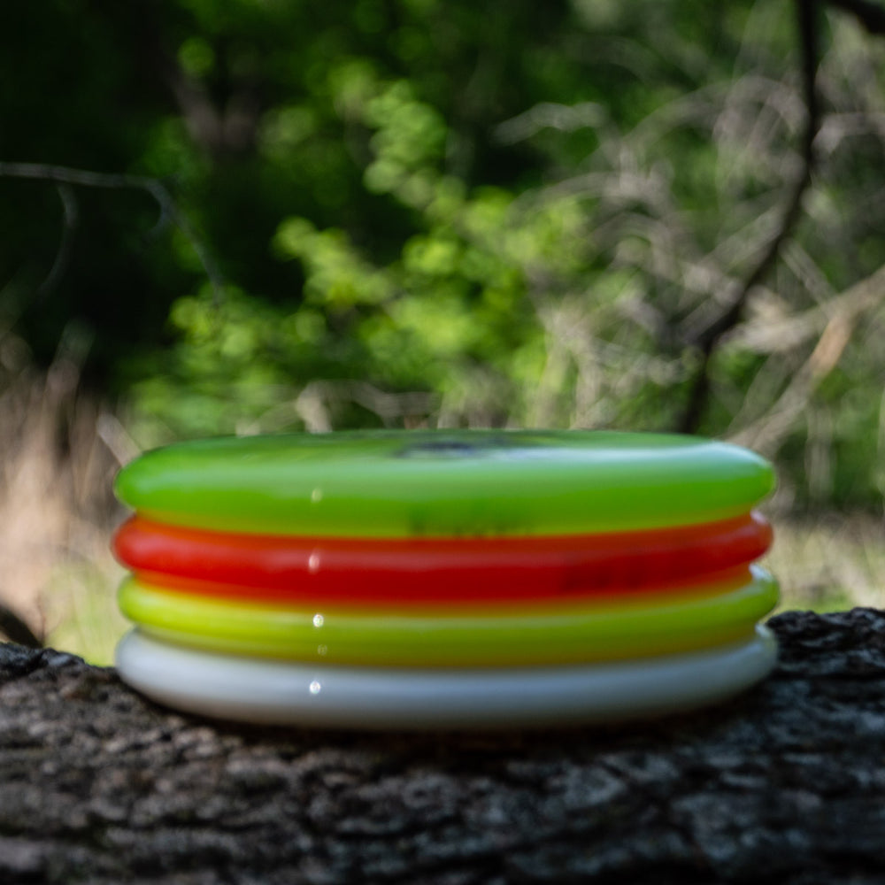 Four brightly colored discs, including a yellow, orange, and white Wizard - Diamond disc, are stacked on a tree trunk against a blurred forest background.