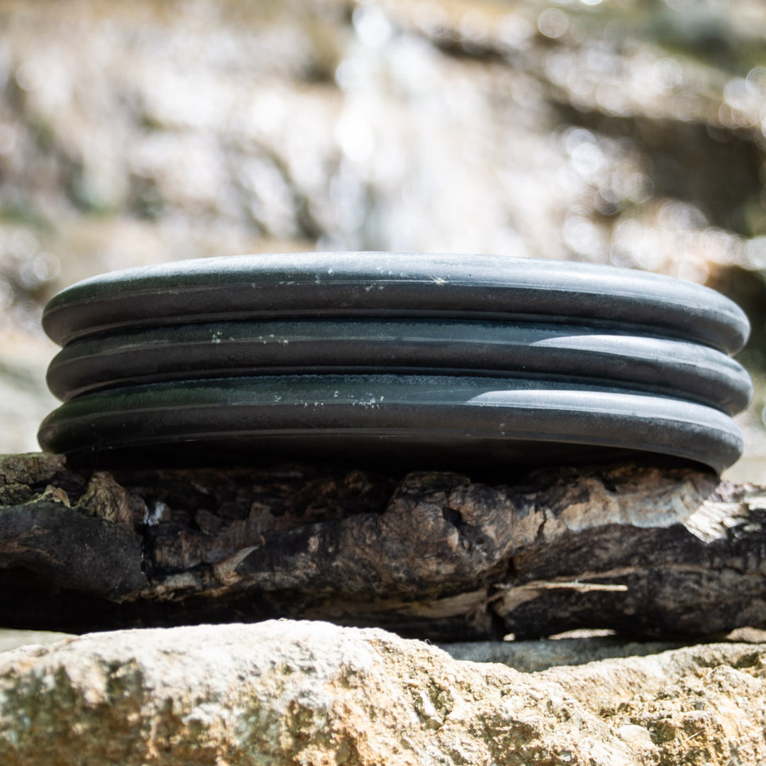 Three stacked Wizard SSS Hearts discs (3 Pack) in black are displayed on a rugged tree branch, surrounded by rocks with a softly blurred natural backdrop.