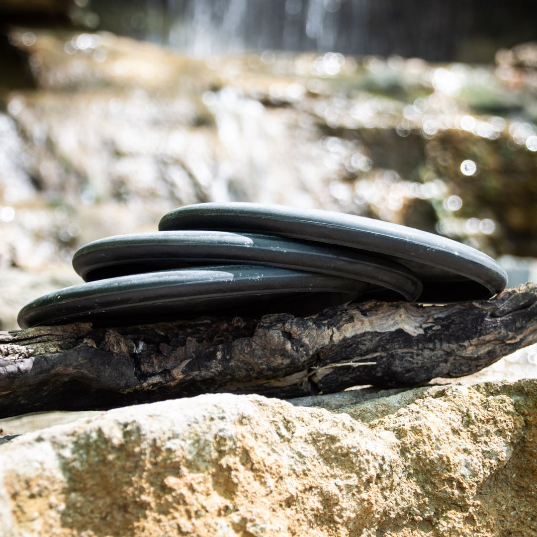 Three Wizard SSS Hearts disc golf discs—renowned for consistency and control—stacked on wood, with rocks and blurred water in the background.