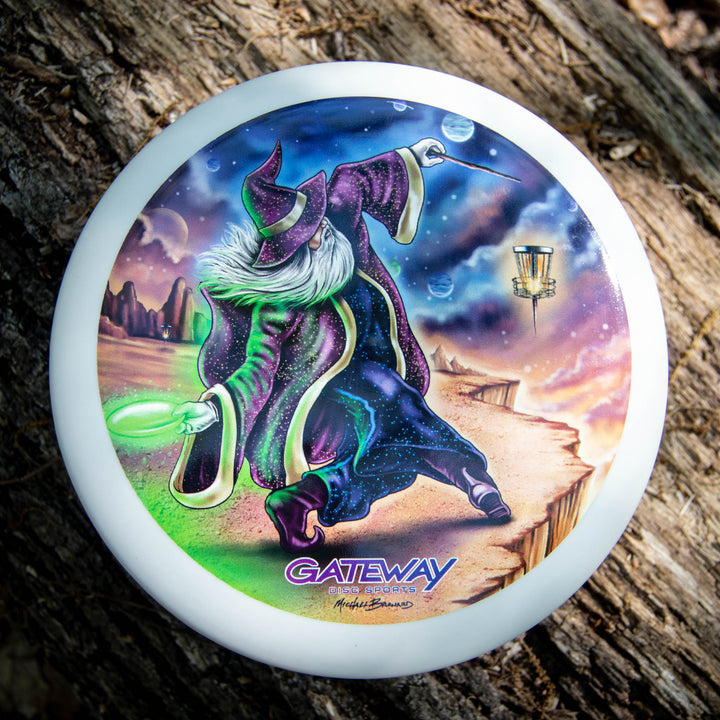 The Wizard - Vivid Color #1 is a white disc golf disc featuring a vivid SSS Wizard illustration of a wizard casting a spell on a cliff, with a basket and desert landscape in the background. Designed by Mike Barnard, "Gateway" is printed at the bottom.