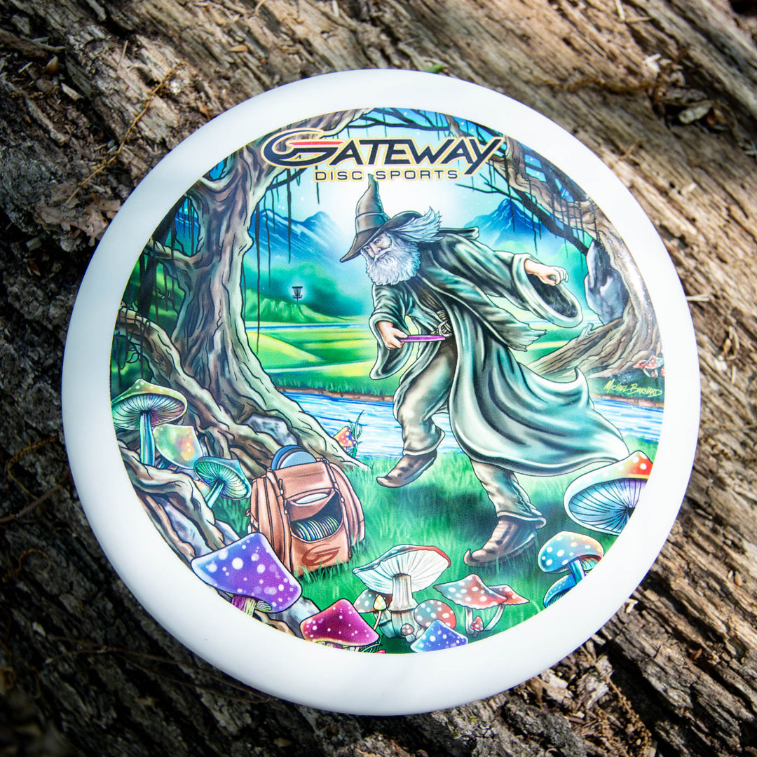 The Wizard - Vivid Color #4 is a white Gateway Disc Sports frisbee featuring a SSS Wizard throwing a disc in a vibrant Mushroom Forest with whimsical mushrooms and tall trees.