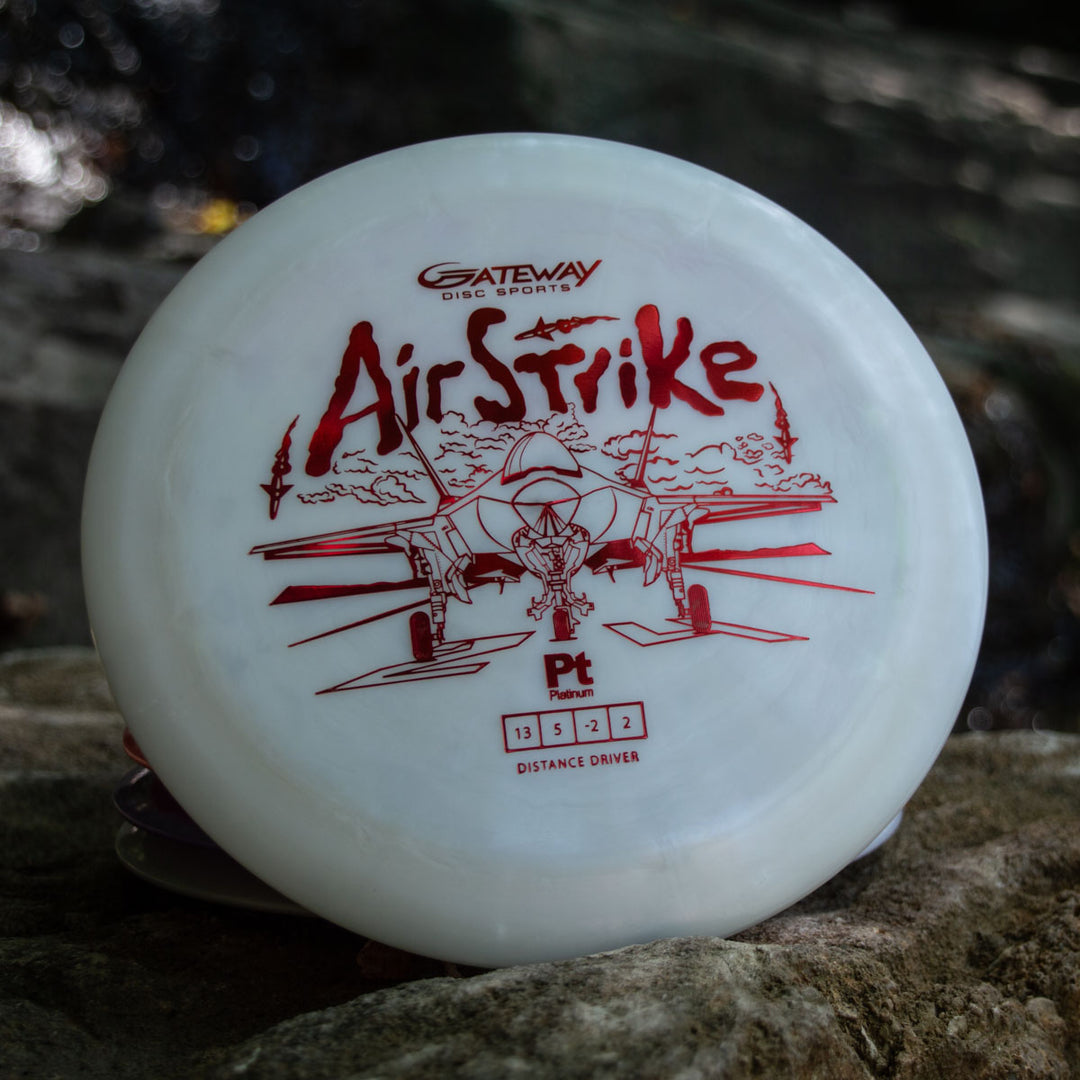 A white Gateway Airstrike - Platinum long range driver with a red airplane graphic and flight numbers, known for its amazing glide, rests on a rock outdoors.