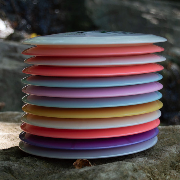 The Airstrike - Platinum long range drivers are stacked on a rock outdoors, providing easy-to-control throws with a colorful look against a blurred natural background.