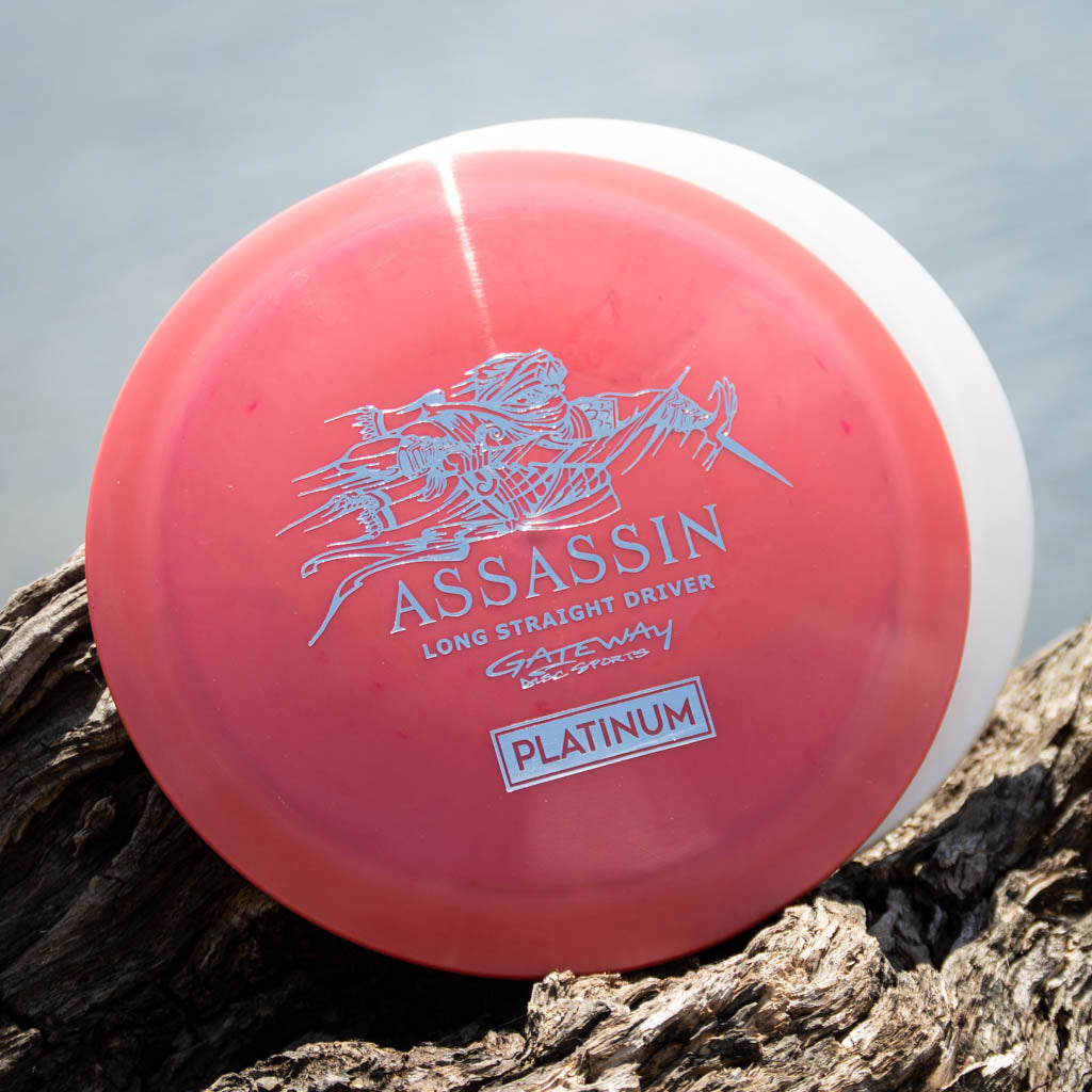 A Gateway Assassin - Platinum distance driver in red and white sits on wood by the water, prized for its excellent glide and neutral flight path.