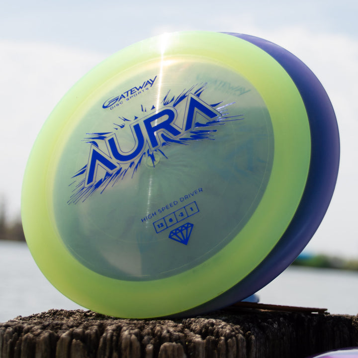 The Aura - Diamond disc golf driver by Gateway Disc Sports stands upright on a weathered wooden post, ready for long, full flights as the less-stable sibling in your bag.
