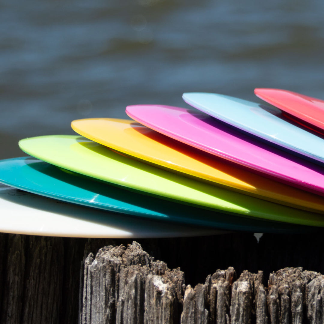 The Aura - Platinum disc golf disc, ideal for smooth turnovers and long flights, rests on a weathered wooden post by the water.