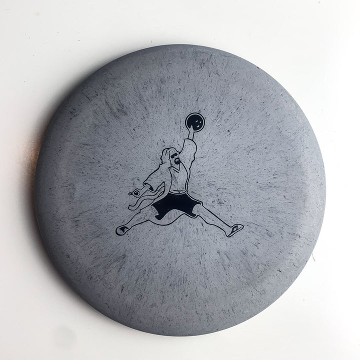 Gray disc with a black outline illustration of a person in mid-air holding a disc, mimicking the "Jumpman" pose—perfect for fans of Gateway Disc Sports putters. Product: Wizard Lunar - Air Dude. Plain white background.