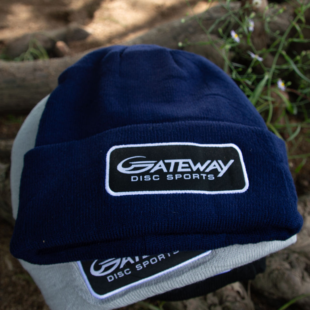 The Gateway Patch Beanie, shown in navy and gray with a "Gateway Disc Sports" patch, is pictured outdoors on dirt—ideal for adding style and warmth to your next tournament players pack.
