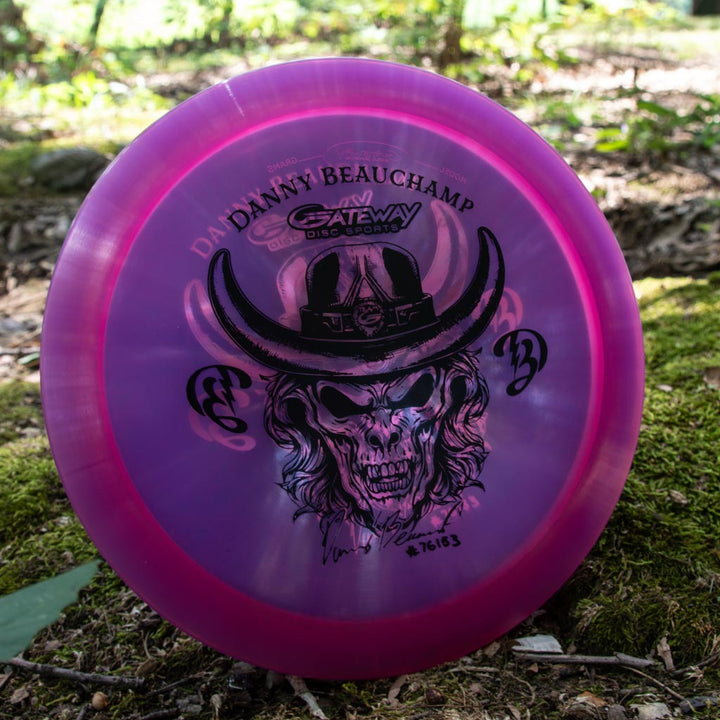A pink overstable Danny Beauchamp Diablo - Diamond fairway driver from Gateway Disc Sports, featuring a black skull-in-cowboy-hat design and branding, is displayed outdoors on mossy ground.