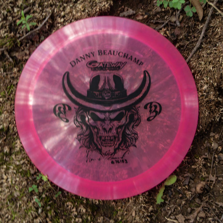 The Danny Beauchamp Diablo - Diamond is a pink overstable fairway driver disc golf disc featuring a skull in a cowboy hat, "Danny Beauchamp" and "Gateway" text, perfect for distance flex shots. Pictured lying on the ground outdoors.