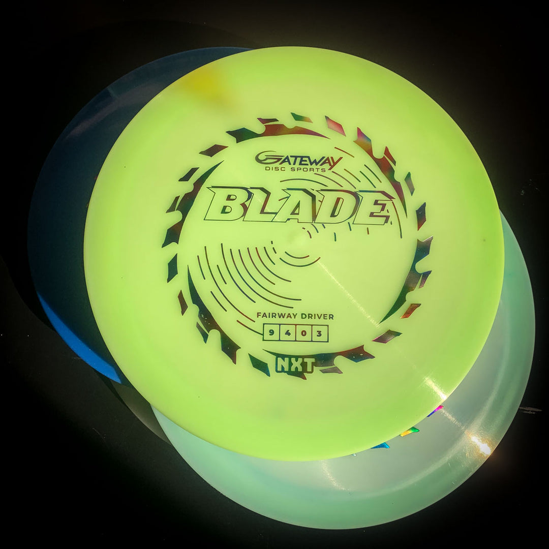 A Blade - NXT overstable fairway driver from Gateway Disc Sports rests atop two colored discs, all illuminated under bright light against a dark background. Perfect for forehand throws, it ensures reliable stability in tough conditions.