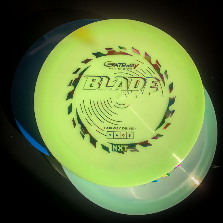 A Blade - NXT overstable fairway driver from Gateway Disc Sports rests atop two colored discs, all illuminated under bright light against a dark background. Perfect for forehand throws, it ensures reliable stability in tough conditions.
