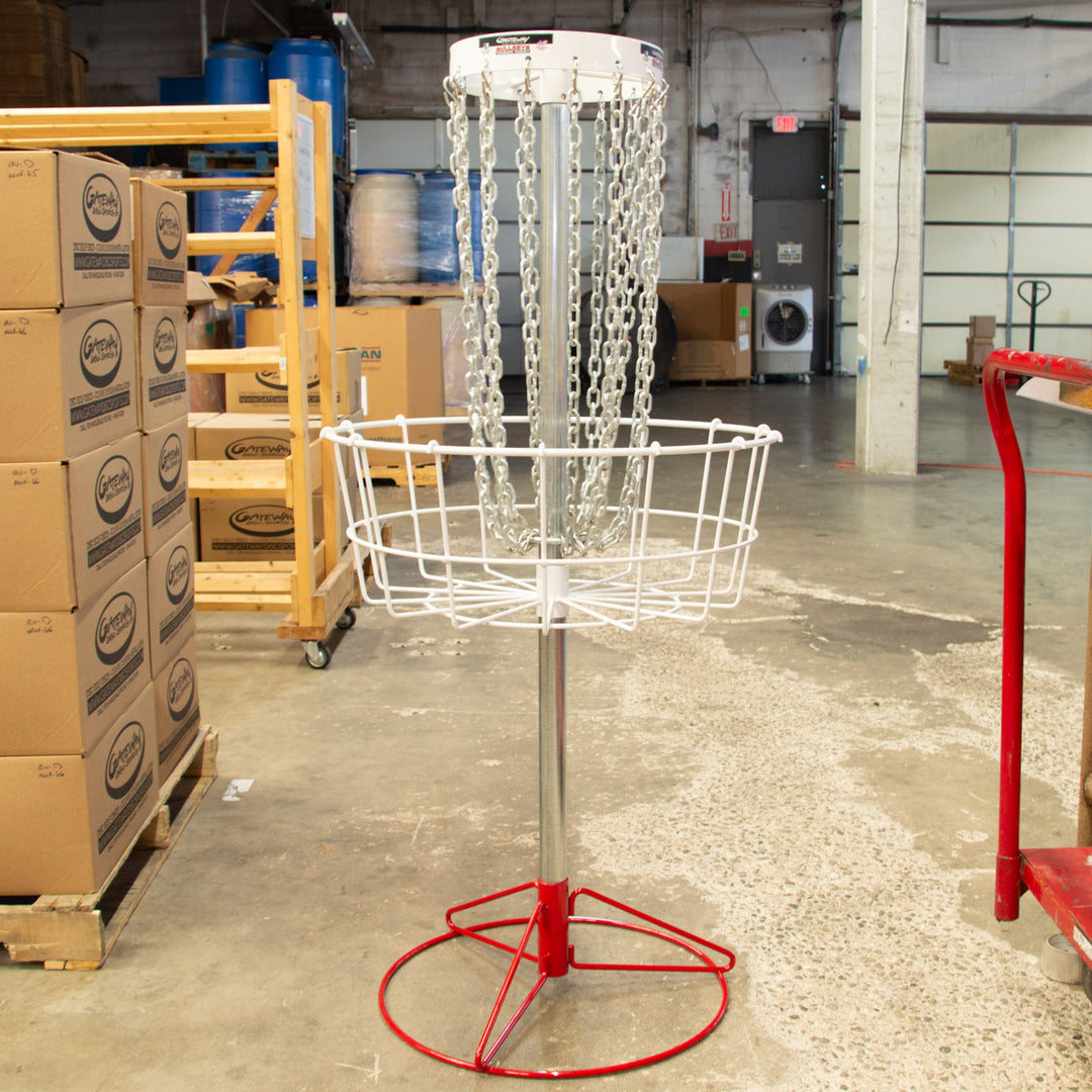 A Bullseye™  Portable Disc Golf Basket, ideal for practice and putting training, stands in a warehouse surrounded by boxes and equipment.