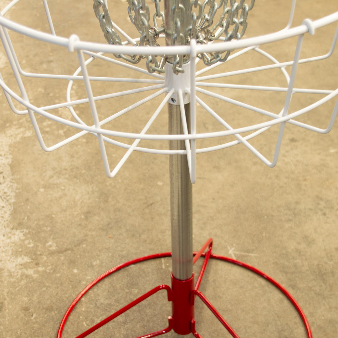 A close-up of the Bullseye™  Portable Disc Golf Basket, showcasing its metal chains and red-and-white frame on concrete—perfect as a disc golf putting trainer for focused practice.