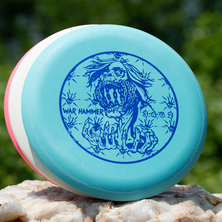 The Black Zombie Warhammer - ZOMBIE — SSSSS is a blue beadless putter disc showcasing a zombie-like creature with an open mouth and skeletal hands.