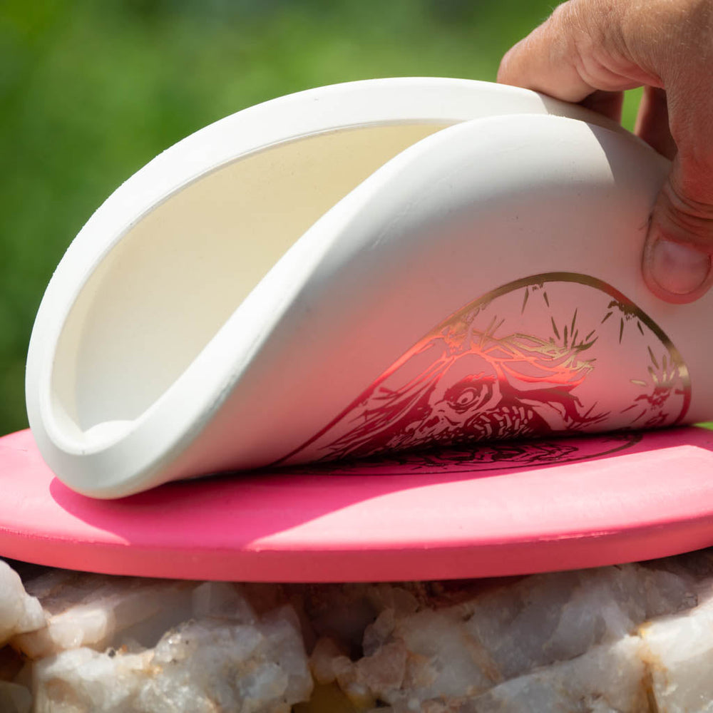 A hand bends a flexible Black Zombie Warhammer - ZOMBIE — SSSS putter featuring a dragon design over a pink disc, outdoors on a sunny day.