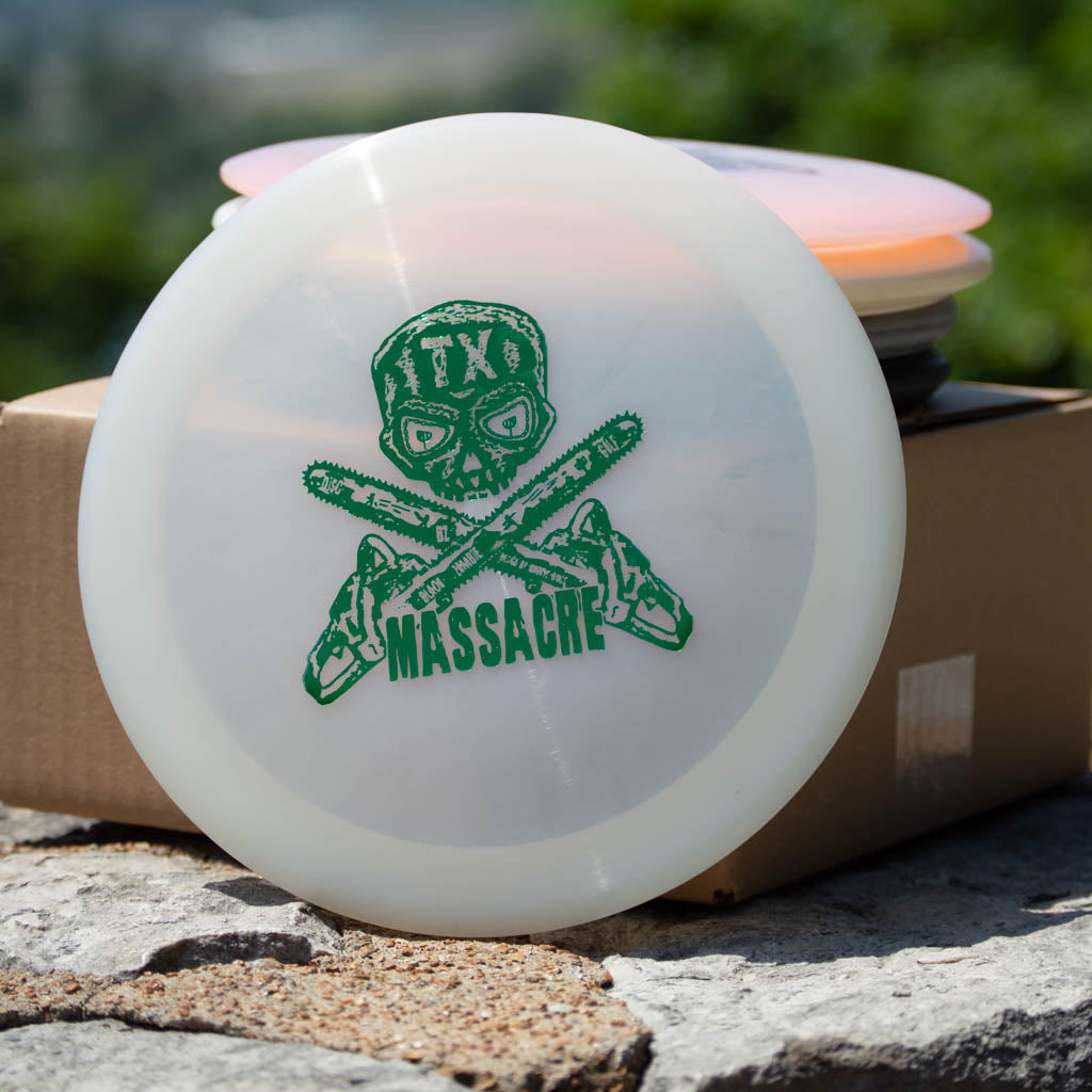 Set of 5 Black Zombie Massacre factory seconds: white disc golf discs with green skull-in-mask above crossed chainsaws and "TX Massacre" text, shown on stone beside a cardboard box.