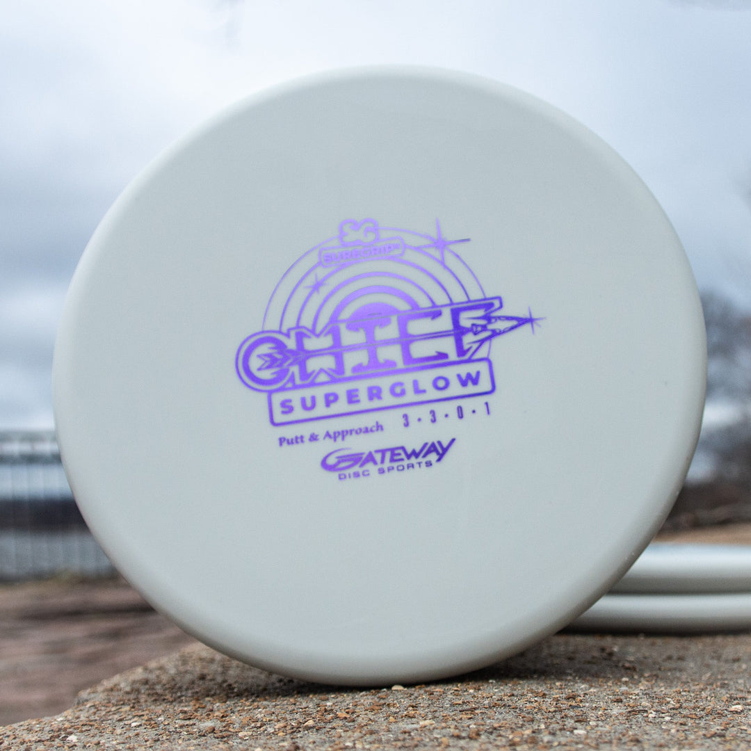 A white low-profile Chief - Suregrip Superglow putter with purple branding sits on a stone surface outdoors.