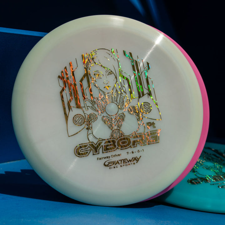 A white Cyborg - Platinum disc golf driver with a holographic cyborg graphic and "CYBORG Fairway Driver 7 6 -3 1 GATEWAY DISC SPORTS" text, known for exceptional glide, rests against a blue background.