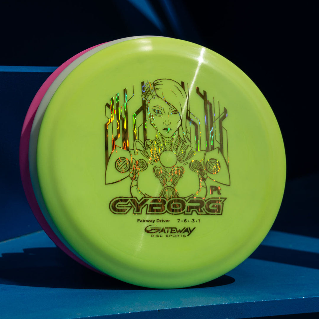 A yellow Cyborg - Platinum fairway driver by Gateway Disc Sports, beginner-friendly with great glide, featuring a cyborg illustration and "CYBORG" text, shown on a blue surface.