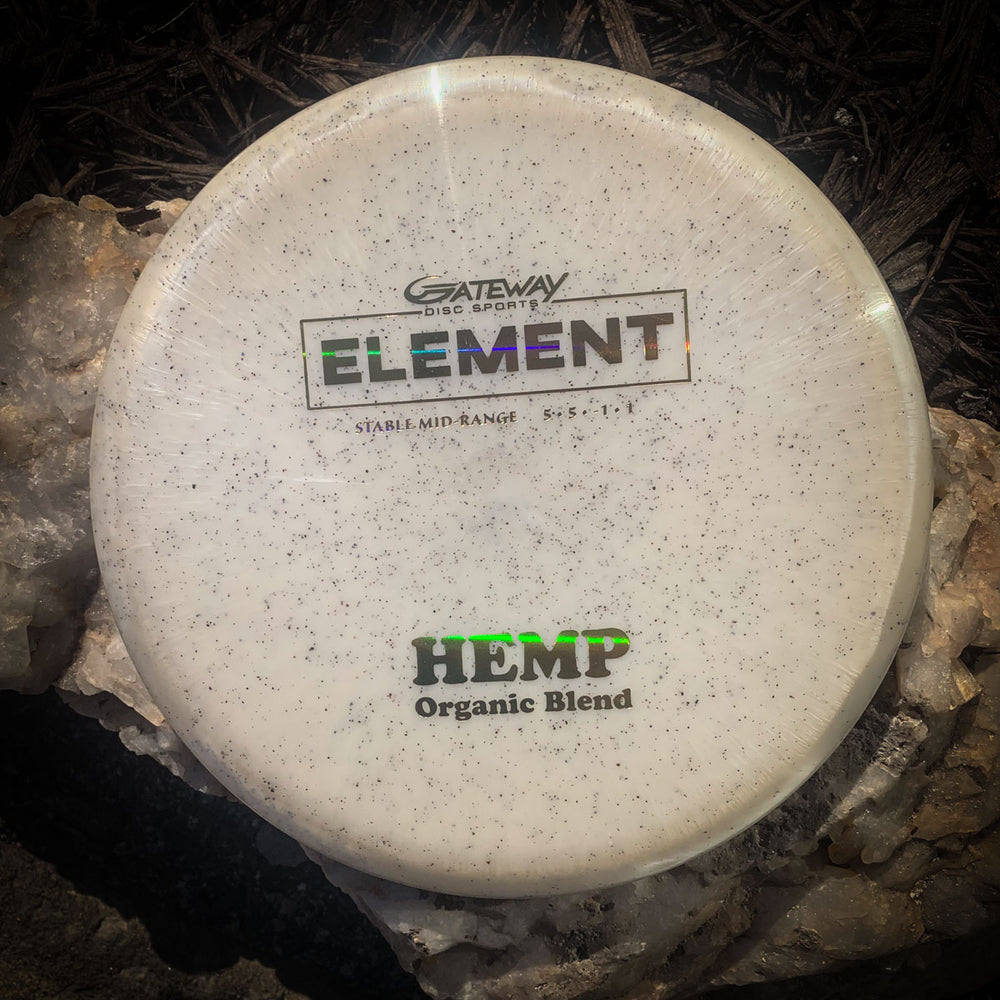 A white Element - Diamond Hemp mid-range disc with "HEMP Organic Blend" and "Stable Mid-Range" text, known for its glide and straight flight, rests on rocks and mulch.