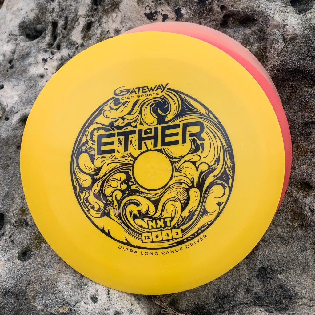 A yellow Ether - NXT (Nylon Xtra Tuff) distance driver by Gateway Disc Sports, PDGA approved with black swirling designs, lies on a textured stone surface.