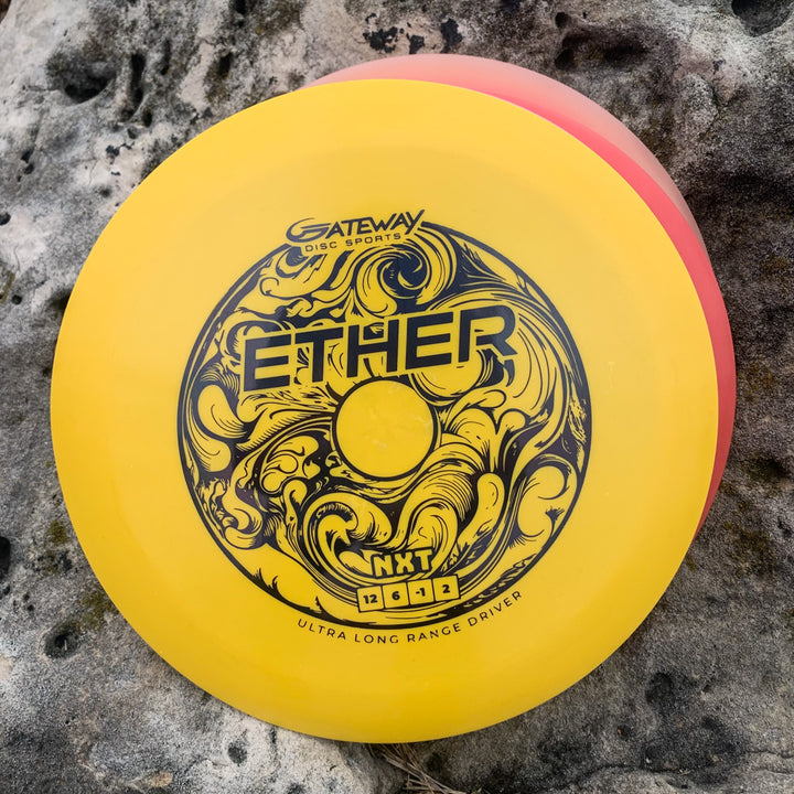 A yellow Ether - NXT (Nylon Xtra Tuff) distance driver by Gateway Disc Sports, PDGA approved with black swirling designs, lies on a textured stone surface.