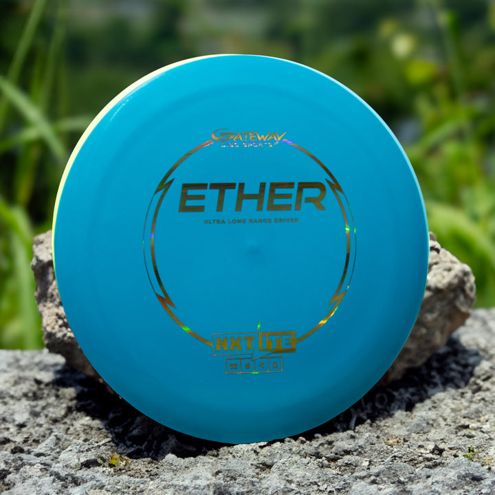 A blue "Ether - NXT LITE" disc golf disc labeled "Ultra Long Range Driver," with Gateway Disc Sports branding and flight numbers, sits on a rock outdoors.