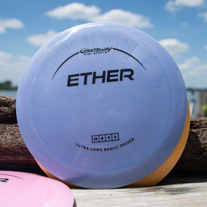 A Gateway Ether - Platinum - First Run distance driver in purple lies on a wooden surface outdoors, with a blue sky and clouds behind it.