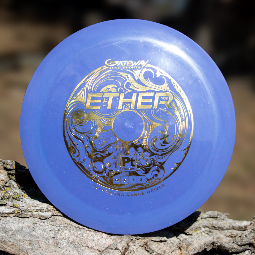 A blue Ether - Platinum - New Run distance driver with gold "Ether" text and manufacturer details, made from eco-friendly plastic, rests on a tree branch.