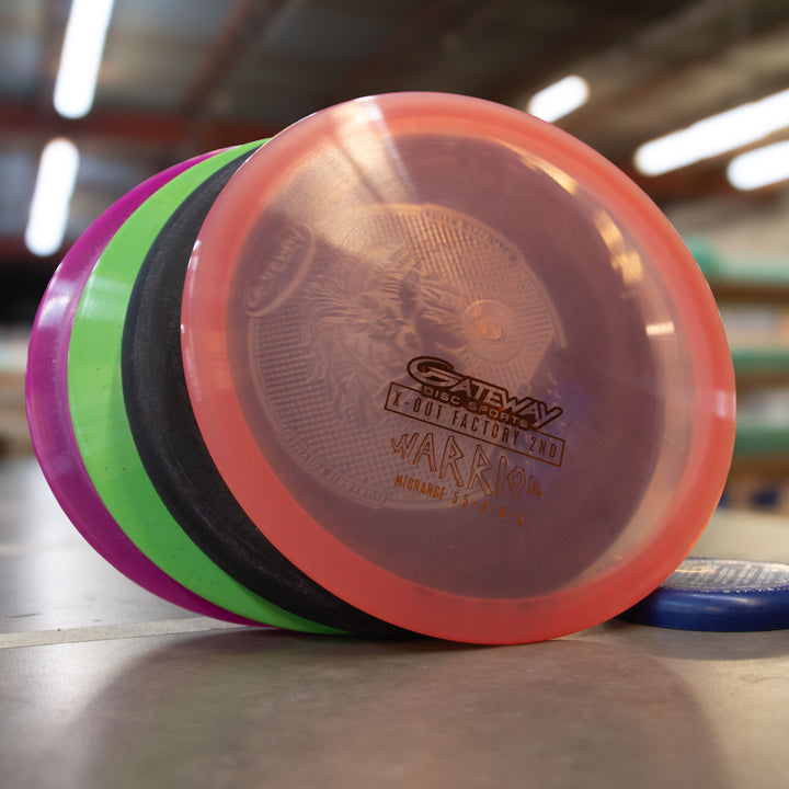 Four Gateway discs from a Factory 2nd 4-Disc Pack are stacked on an indoor table, with the top disc labeled "Gateway Disc Sports Warrior." Shelves and lights can be seen in the background.