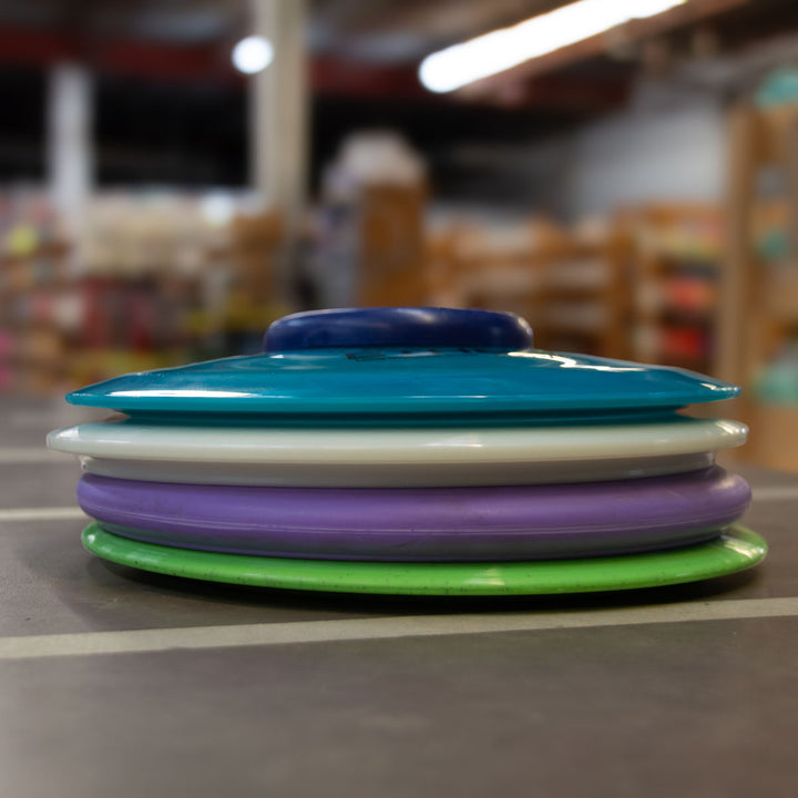 A stack of colorful discs from the Factory 2nd 4-Disc Pack sits on a table inside a store, with shelves of products visible in the blurred background.