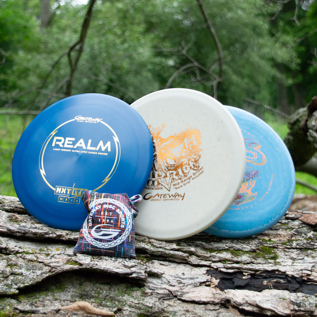 The Father's Day Gift Set, which includes three disc golf discs and a third place prize bag, sits on a large log with a lush green forest in the background.