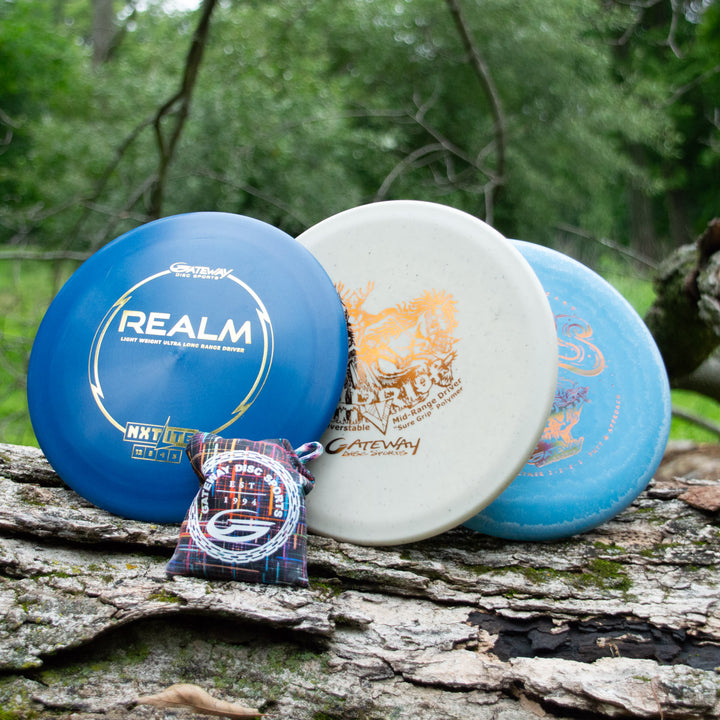 The Father's Day Gift Set, which includes three disc golf discs and a third place prize bag, sits on a large log with a lush green forest in the background.