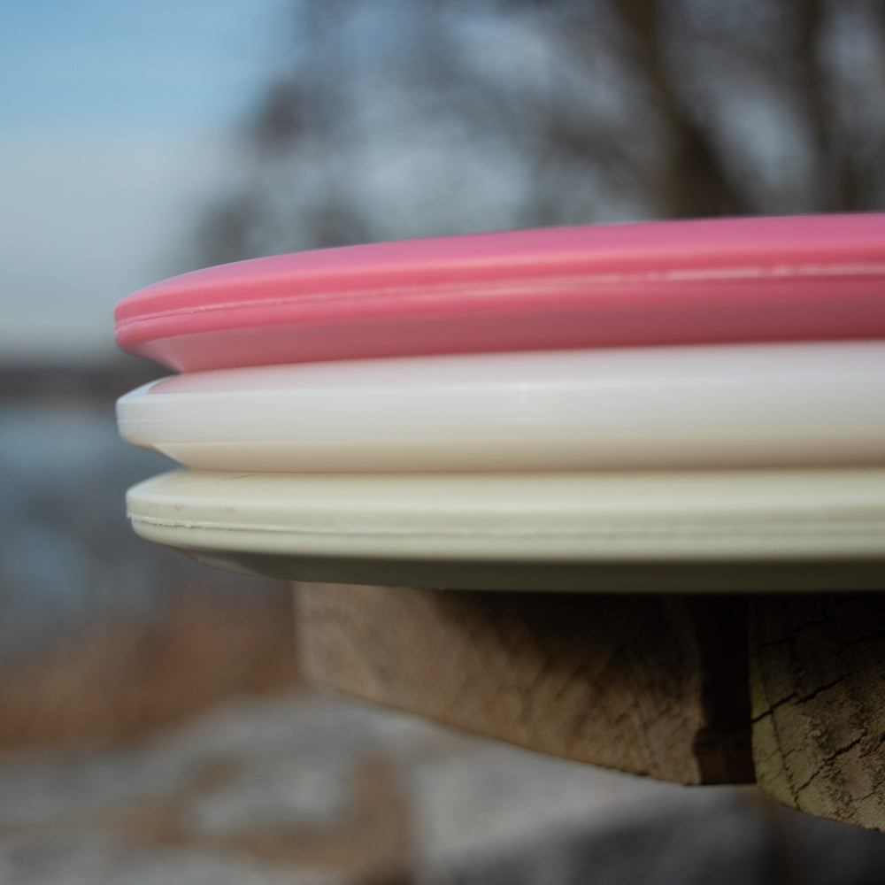 Three stacked Full Turn Guide - Express discs—pink, white, and off-white—rest on a wooden surface outdoors, neatly arranged like flight numbers against a softly blurred natural backdrop.