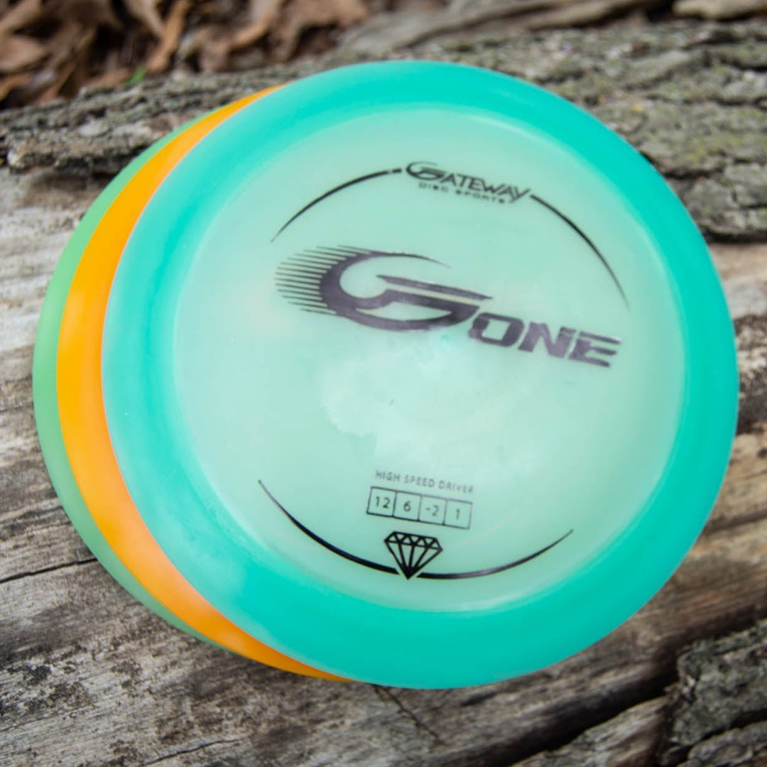 A G-One distance driver disc golf disc with teal and orange edges rests on textured wood.