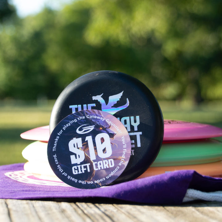 A $10 gift card sits atop the Gateway Gauntlet - 3 Disc Players Pack outdoors, ideal for your next disc golf tournament, with a blurred green background.