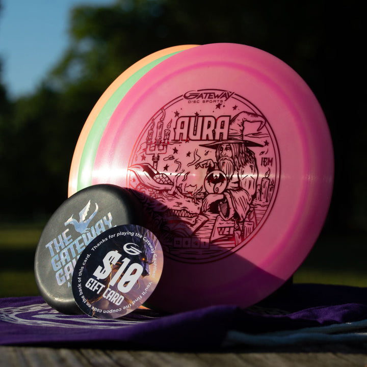 A Gateway Gauntlet - 3 Disc Players Pack and an $18 Gateway gift card rest on a purple cloth outdoors with greenery in the background—ideal prizes for any disc golf tournament or fans of new discs from Gateway Disc Sports.