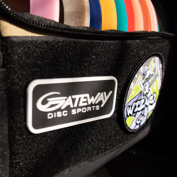 Close-up of a black bag featuring the Gateway Velcro Logo Patch, partially unzipped to reveal colorful disc golf discs inside.