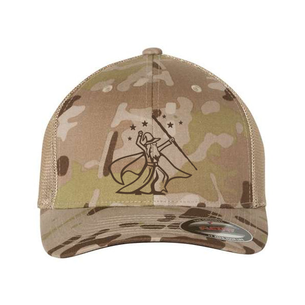 The Wizard Flexfit Fitted Trucker Cap is a tan Multicam camo cap with a black graphic of a caped figure holding a flag and five stars on the front, featuring an elastic band for comfort and a snug fit.