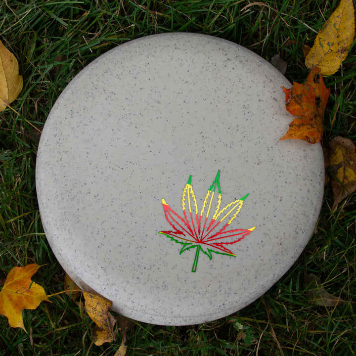 The Wizard - SS Hemp - Leaf from Gateway Disc Sports is a gray putter with a red, yellow, and green leaf design, pictured on grass amid autumn leaves—ideal for highlighting this disc's unique hemp-infused plastic blend.