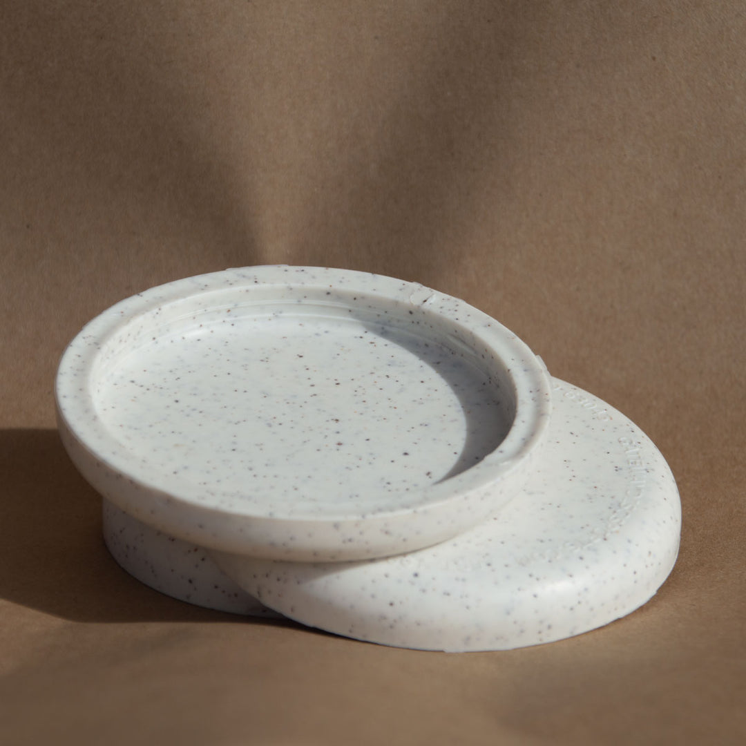 Two round, white speckled Mini (Small) - Hemp - Blank coasters are stacked on a brown background, with one leaning against the other—perfect for use as eco-friendly custom mini markers at stylish promotional events.