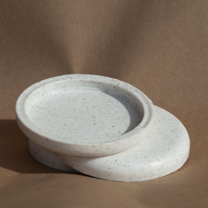 Two round, white speckled Mini (Small) - Hemp - Blank coasters are stacked on a brown background, with one leaning against the other—perfect for use as eco-friendly custom mini markers at stylish promotional events.