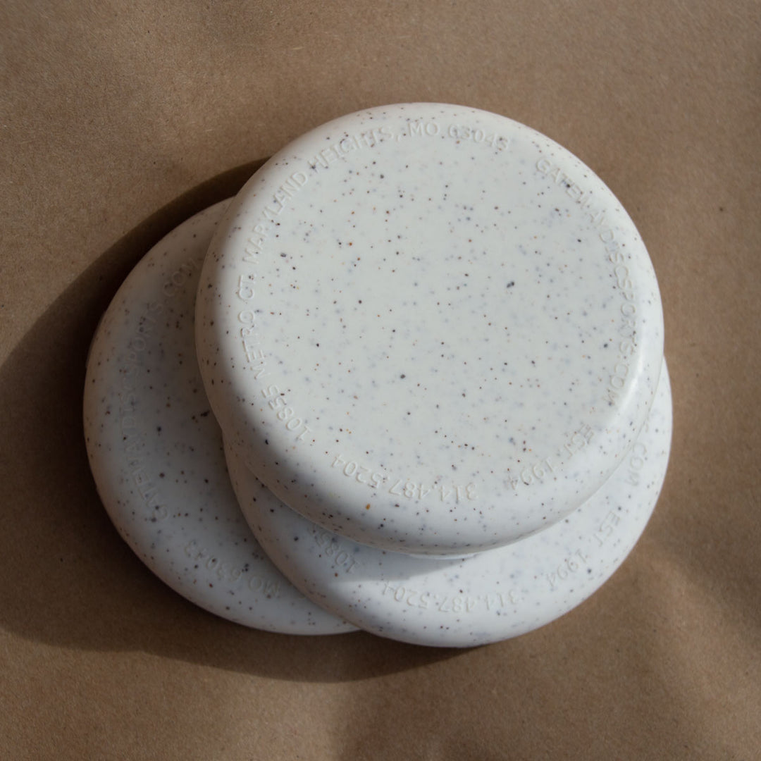 Three round, speckled white Mini (Small) - Hemp - Blank soap bars are stacked on brown paper€”ideal as distinctive promotional giveaways.
