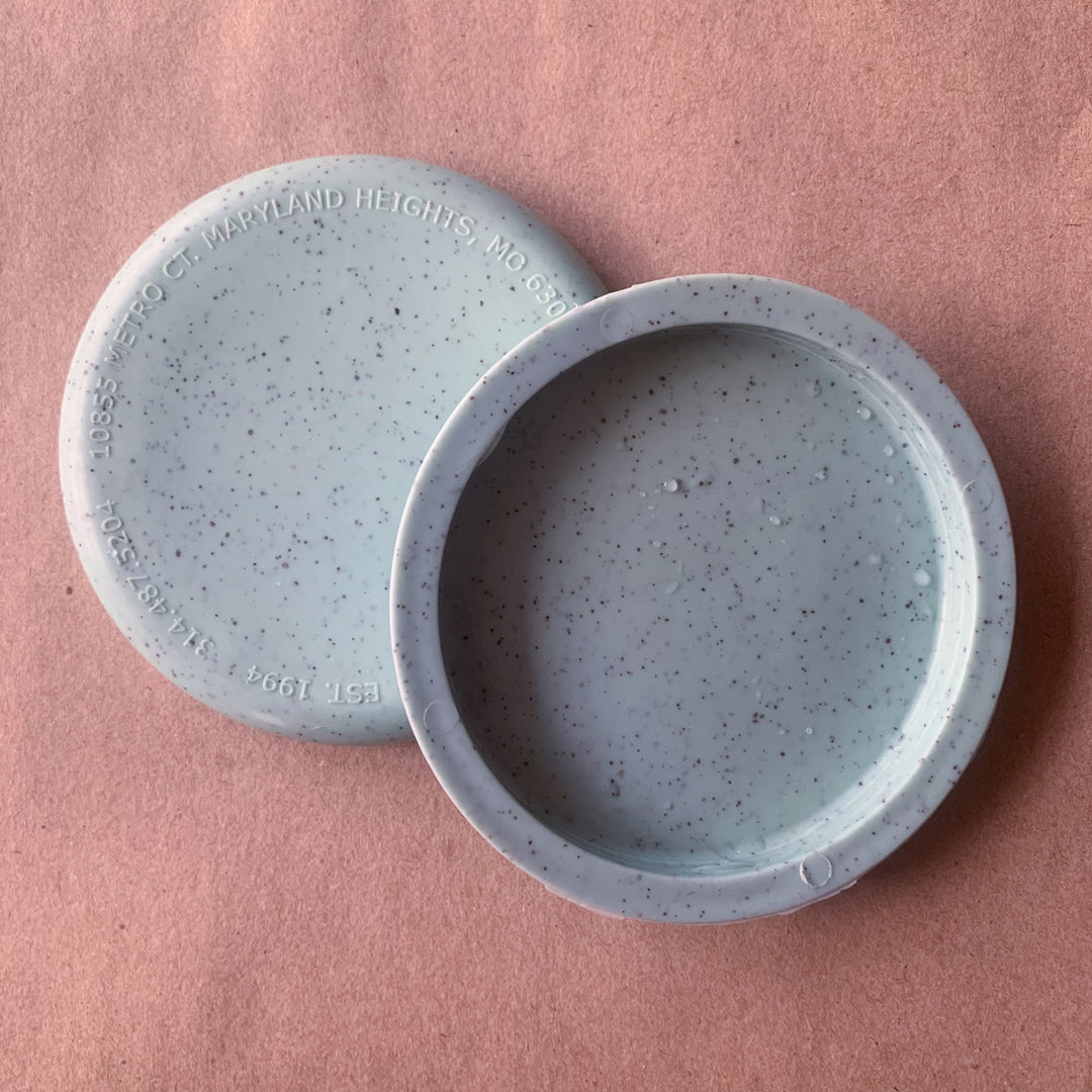 Two round, speckled light gray Mini (Small) - Hemp - Blank coasters are displayed on a textured pink surface, one flat and one leaning for visual interest—perfect for unique promotional giveaways.